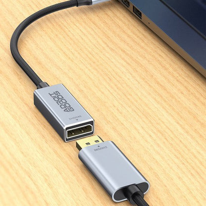Grijze USB-C naar DisplayPort adapter aangesloten op een laptop op een houten oppervlak.