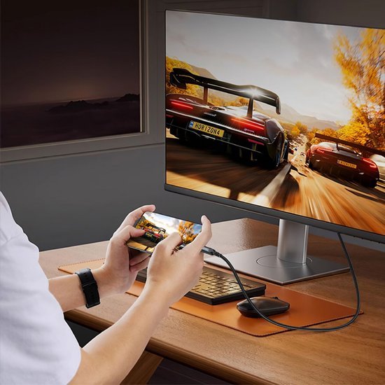 Persoon speelt racegame op smartphone verbonden met groot computerscherm op bureau in kamer