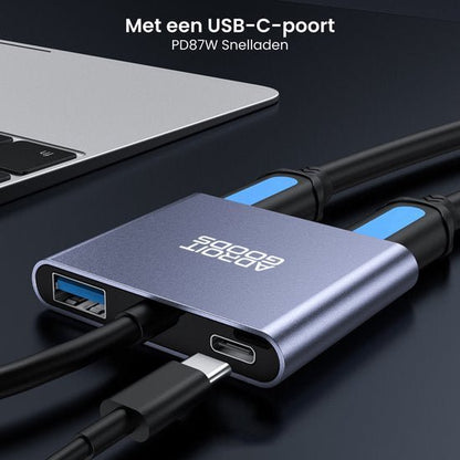 Compact metalen adapter met USB-C- en USB-A-poorten en twee aangesloten kabels naast laptop