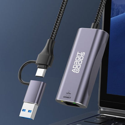 Grijze AdroitGoods adapter met USB en ethernet aansluiting naast laptop aansluitpoort.