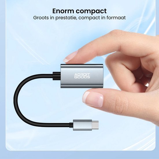 Hand houdt compacte zilverkleurige AdroitGoods adapter met USB-C kabel tegen blauwe achtergrond