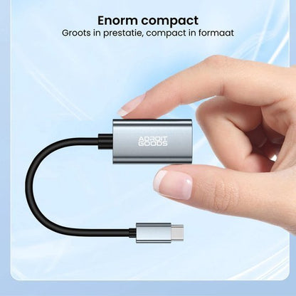 Hand houdt compacte zilverkleurige AdroitGoods adapter met USB-C kabel tegen blauwe achtergrond