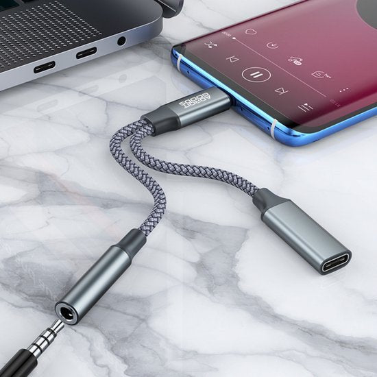 Draadloze audioadapter met gevlochten kabel verbonden met smartphone en laptop op marmeren oppervlak