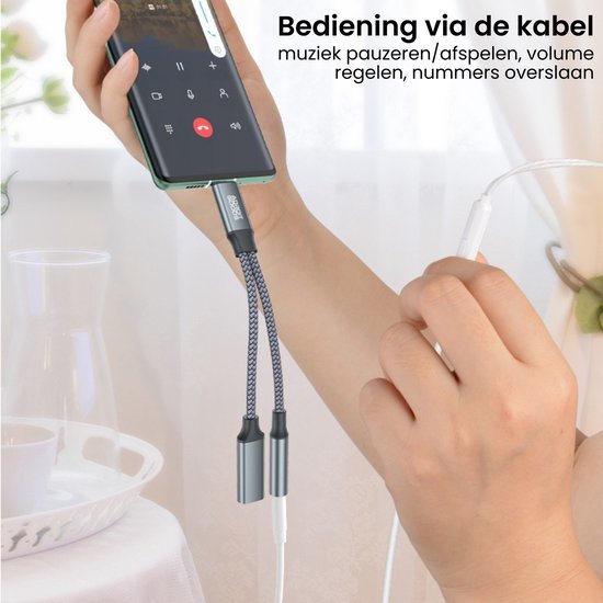 Hand houdt smartphone met dubbele kabeladapter en bedrade oordopjes in lichte kameromgeving