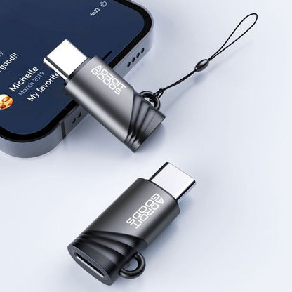 Zwarte en grijze USB-C adapters met AdroitGoods logo en koordje naast smartphone