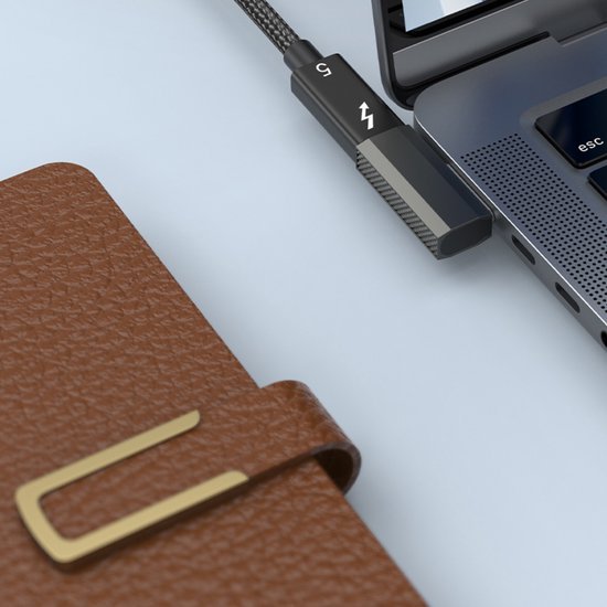 Zwarte gevlochten kabel aangesloten op laptop naast bruin lederen notitieboek met gouden gesp