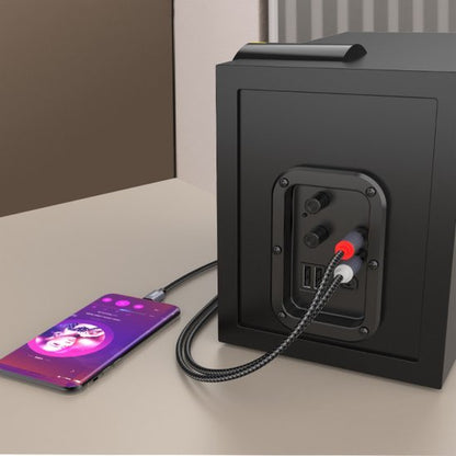 Smartphone aangesloten op een zwarte luidspreker met rode en witte audiokabels op een tafel.