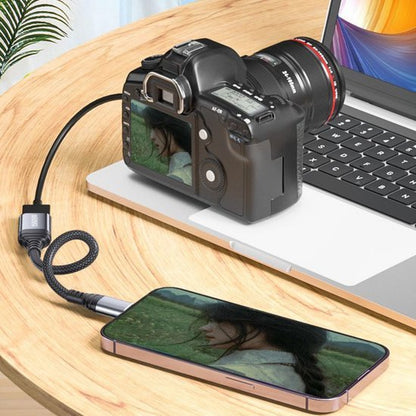 Camera aangesloten op laptop en smartphone via een zwarte USB-kabel op houten tafel
