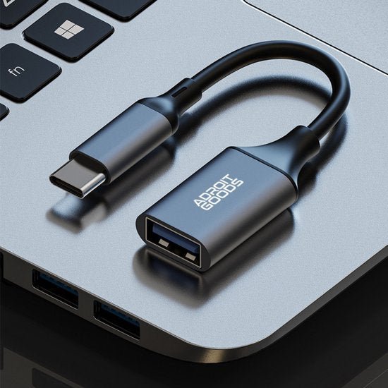 Zwarte USB-C naar USB-A adapter aangesloten op een zilveren laptop met AdroitGoods logo