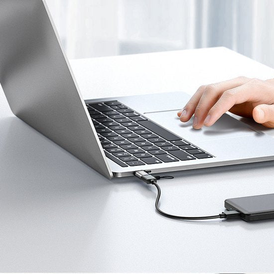 Hand die de trackpad bedient van een laptop aangesloten op een externe harde schijf via een kabel