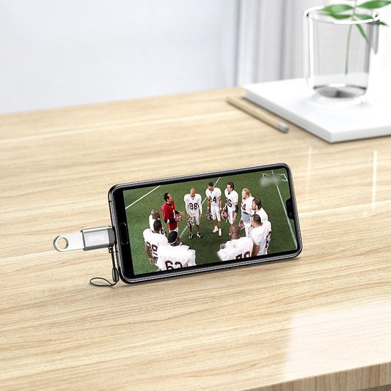 Smartphone met USB-stick die sportteam toont, geplaatst op houten bureau naast kopje planten