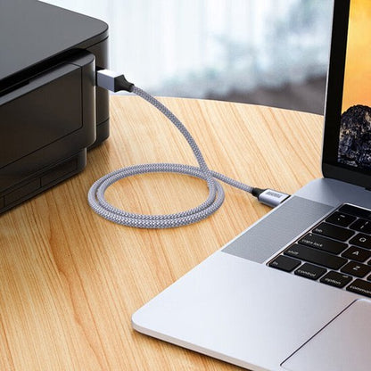 Grijs gevlochten USB-C-kabel verbonden tussen laptop en printer op houten bureau.
