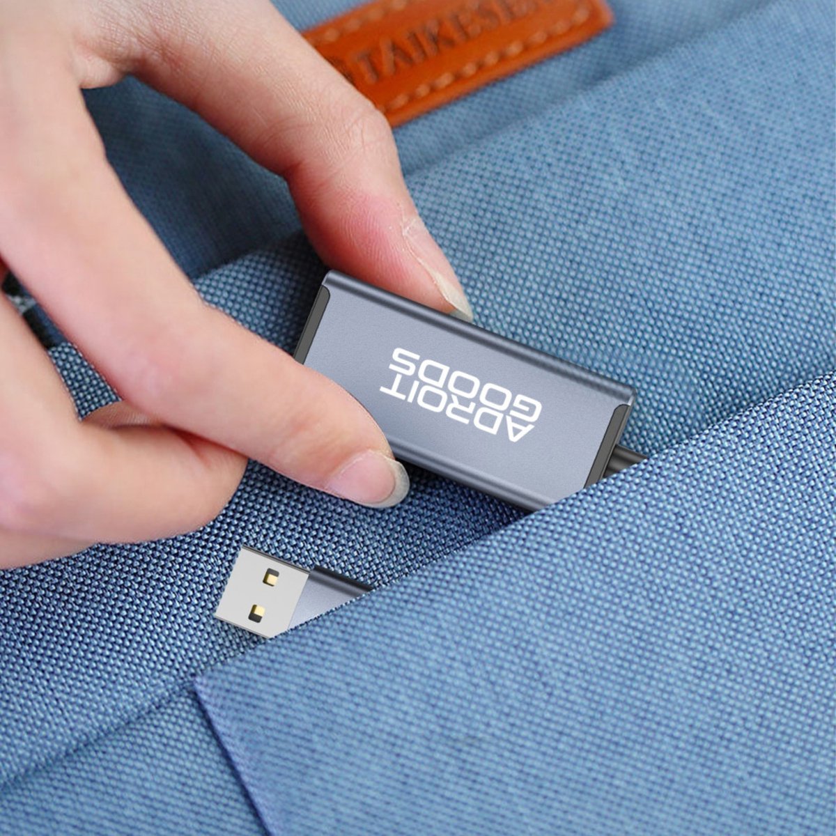 Hand die een grijze AdroitGoods USB-stick uit een blauw stoffen zakje haalt.