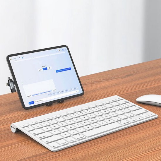 Draadloos wit toetsenbord en muis naast een tablet op een houten bureau in lichte kamer