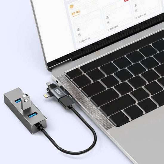 Zilverkleurige USB-hub met drie poorten aangesloten op een zilveren laptop met zwart toetsenbord.