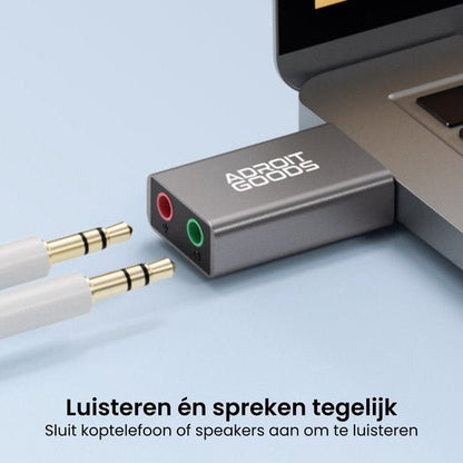 Zilverkleurige adapter met twee audiopoorten aangesloten op een laptop voor geluid en microfoon.
