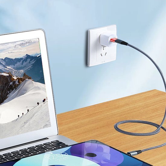 Oplaadkabel verbonden met een wandcontactdoos en elektronische apparaten op een houten tafel.