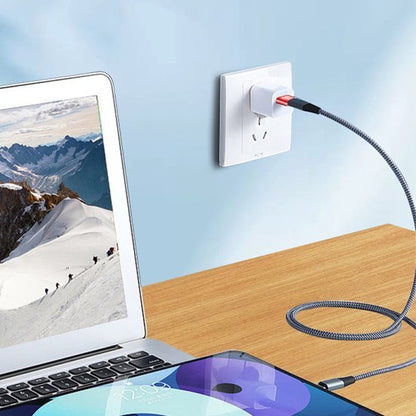 Oplaadkabel verbonden met een wandcontactdoos en elektronische apparaten op een houten tafel.