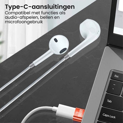 Witte oordopjes met Type-C aansluiting naast een laptop op een donkere ondergrond