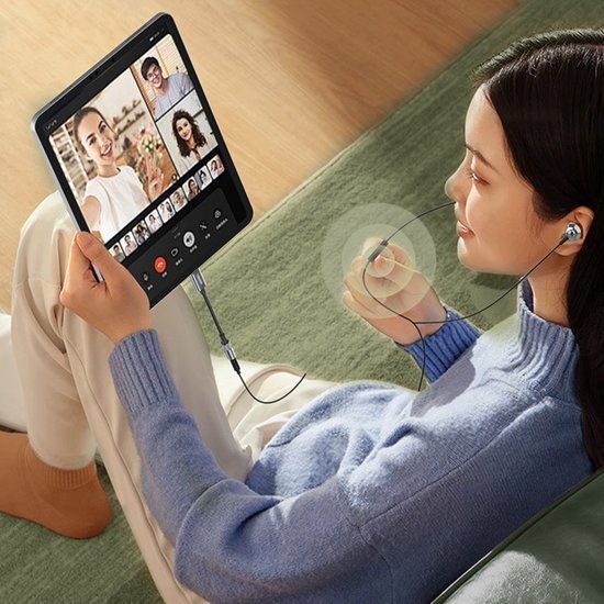 Vrouw zittend op bank met koptelefoon en videochat op tablet in ontspannen omgeving