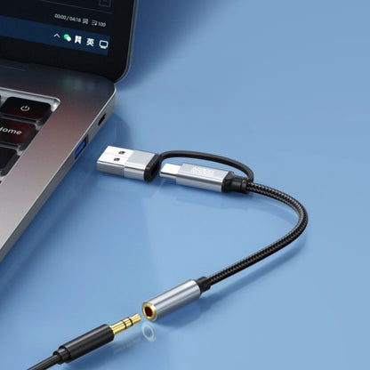 Zwarte en zilveren USB- naar 3,5 mm audiokabel naast een laptop op een lichte ondergrond