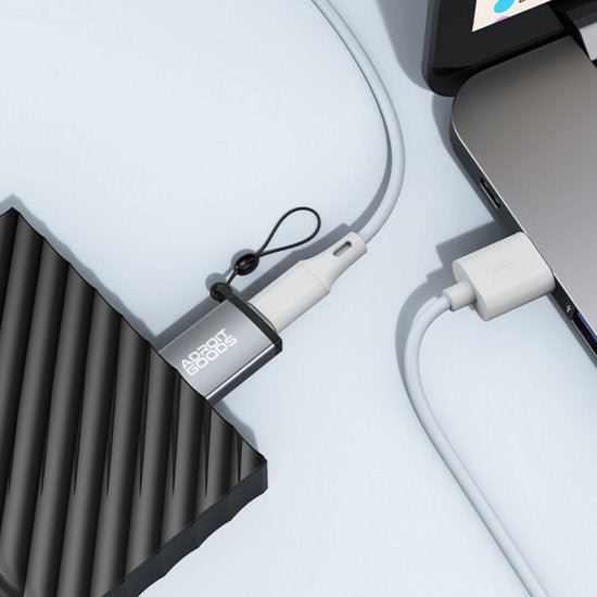 Zwarte externe harde schijf aangesloten op laptop met wit oplaadkabeltje en sleutelhanger