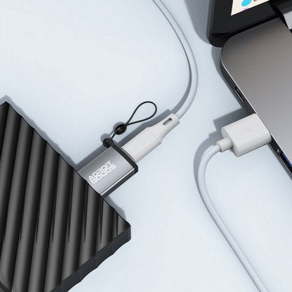 Zwarte externe harde schijf aangesloten op laptop met wit oplaadkabeltje en sleutelhanger