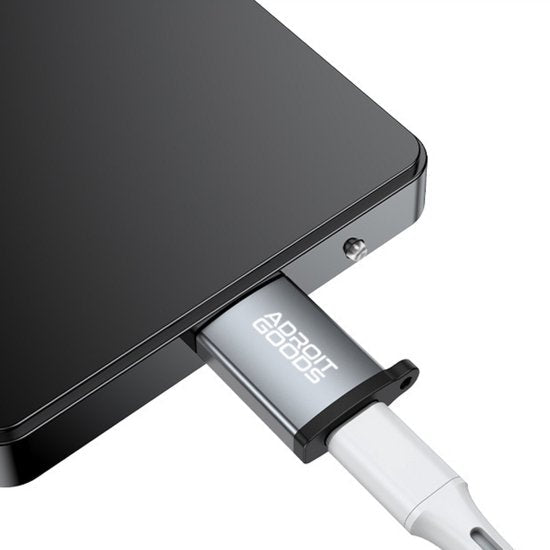 Zilveren AdroitGoods adapter aangesloten op een zwart elektronisch apparaat met witte kabel.