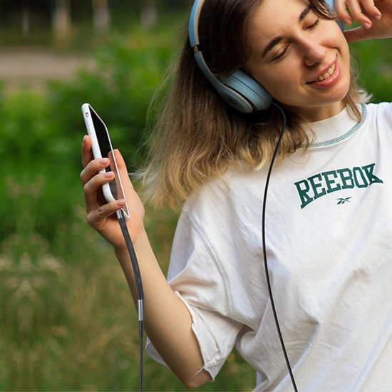 Vrolijke jonge vrouw geniet van muziek met grote koptelefoon en smartphone in hand buiten