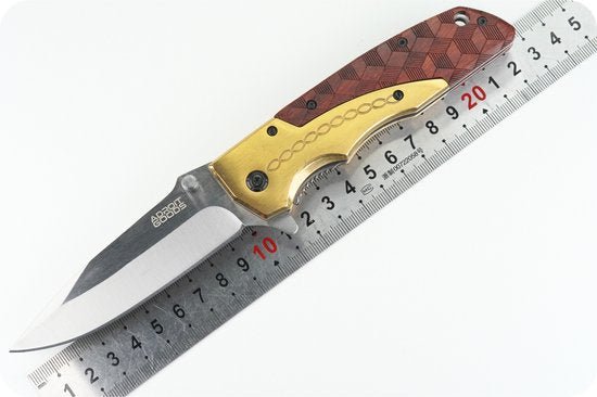 Opvouwbaar mes met houten en gouden handvat naast een liniaal voor lengtevergelijking