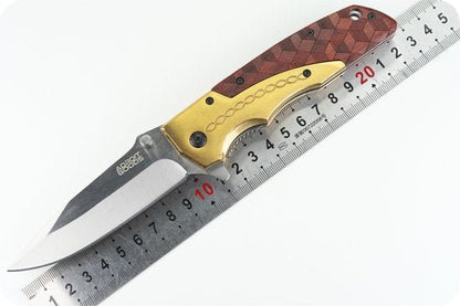 Opvouwbaar mes met houten en gouden handvat naast een liniaal voor lengtevergelijking