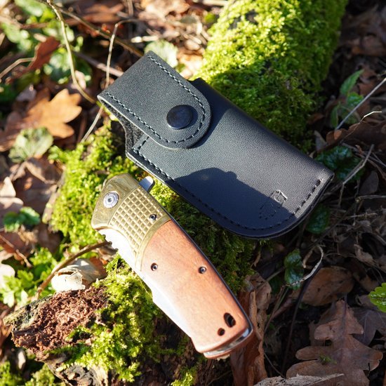 Zakmes met houten handvat naast een zwart leren hoesje op mosgrond in het bosgebied