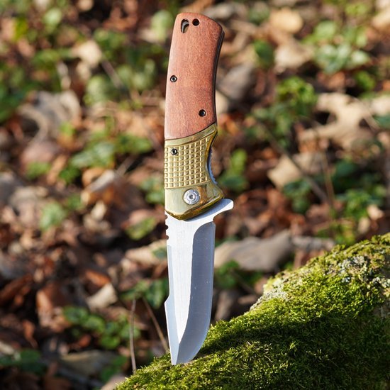 Opengeslagen zakmes met houten handvat en metalen lemmet in een bosrijke omgeving geplaatst.