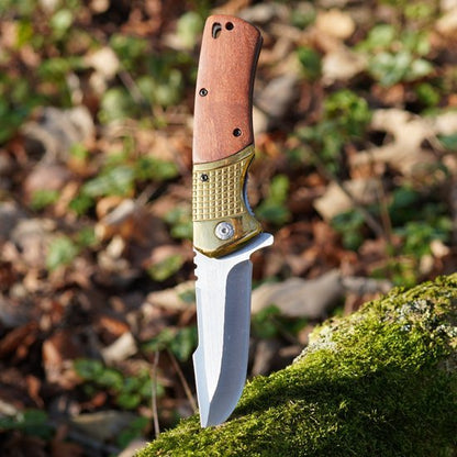 Opengeslagen zakmes met houten handvat en metalen lemmet in een bosrijke omgeving geplaatst.