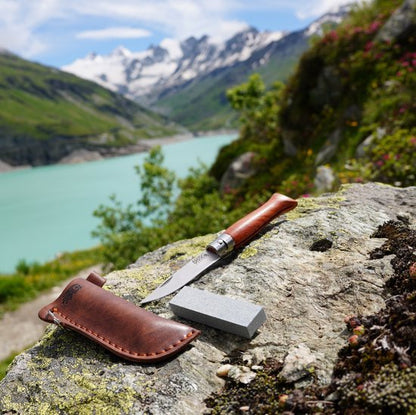 Zakmes met houten handvat en leren schede op rots met rivier en bergen op de achtergrond