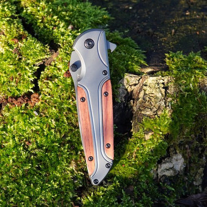 Gesloten inklapbaar mes met houten handgreep liggend op mos en boomschors in natuurlijk licht.