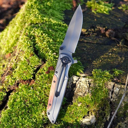 Opvouwbaar mes met houten handvat ligt op een met mos bedekte boomstronk in het bos