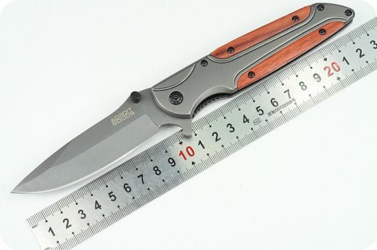 Opvouwbaar mes met houten handgreep en metalen lemmet op een meetlat geplaatst