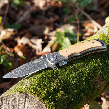 Opengeslagen mes met houtgreep en gegraveerd lemmet op mosgroene boomstam in natuur