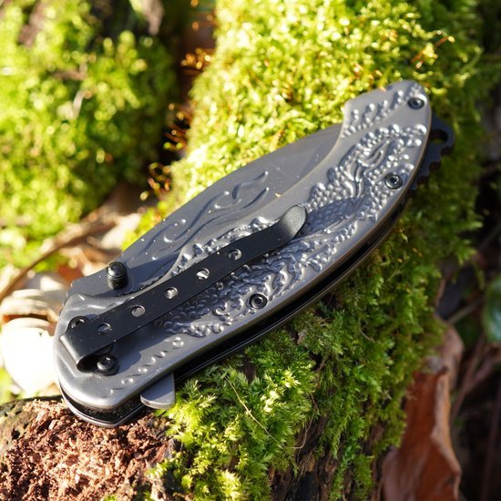 Opgevouwen zakmes met gedetailleerd handvat liggend op mosgroene bosgrond