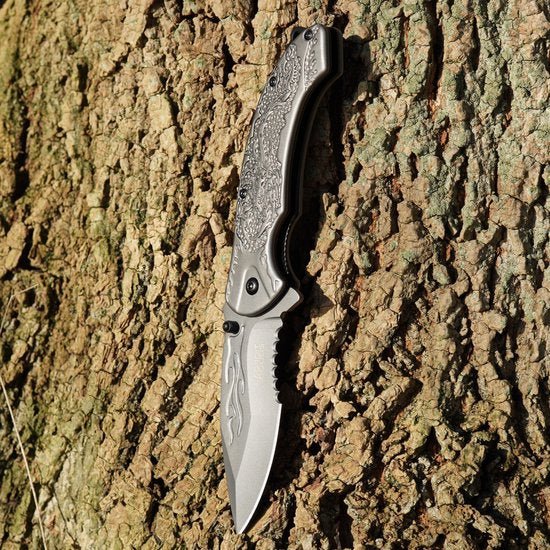 Opvouwbaar mes met gegraveerd handvat tegen boomschors achtergrond in natuurlijk licht