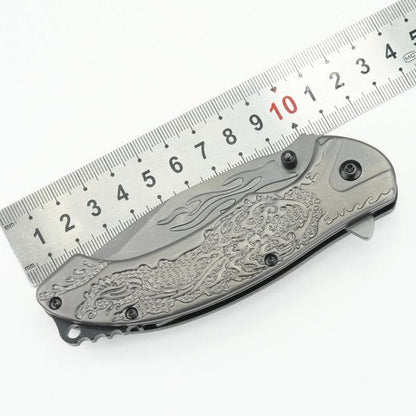 gesloten metalen zakmes met gedetailleerd draakpatroon en liniaal op witte achtergrond