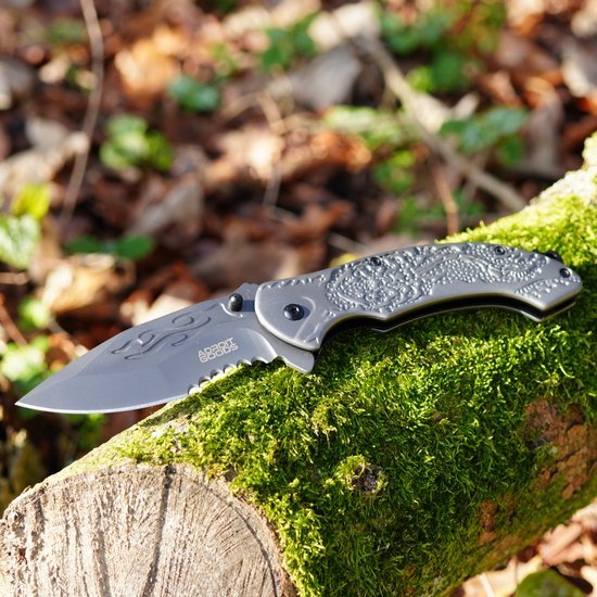 Opgevouwen zakmes met gegraveerd lemmet en handgreep op mosbedekte boomstronk in bosrijke omgeving