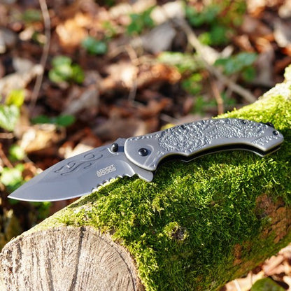 Opgevouwen zakmes met gegraveerd lemmet en handgreep op mosbedekte boomstronk in bosrijke omgeving